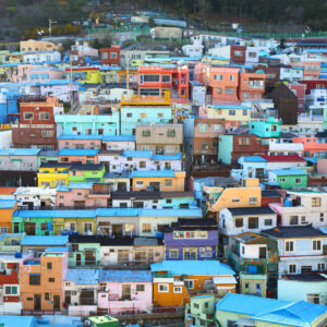 Casas coloridas e vibrantes no Gamcheon Culture Village, em Busan, Coreia do Sul, dispostas em camadas na encosta de uma colina, com o céu azul no fundo.