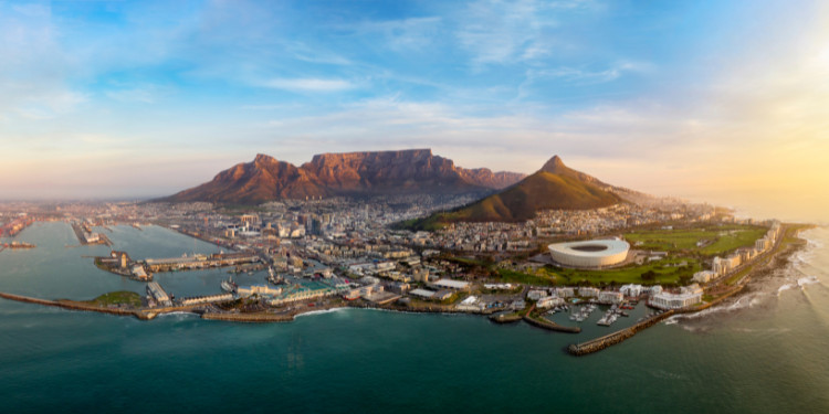 Fotografia aérea da Cidade do Cabo, África do Sul, mostrando a Table Mountain ao fundo, a costa com o Oceano Atlântico, edifícios da cidade e o Cape Town Stadium.