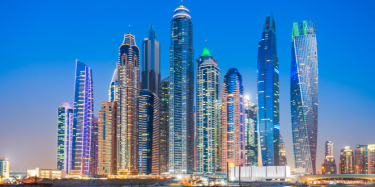 Paisagem urbana de Dubai com arranha-céus de vidro e aço, palmeiras, áreas verdes e o Burj Khalifa, o prédio mais alto do mundo, ao fundo.