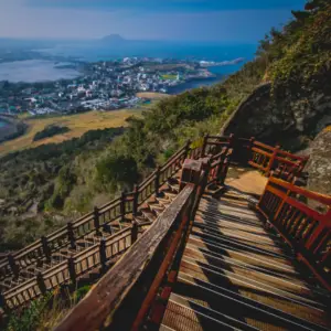 Escadaria de madeira íngreme em Seogwipo, com vista para a cidade e o mar ao fundo.