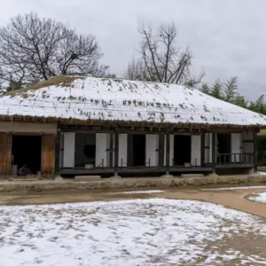 Casa tradicional coreana com telhado de palha coberto de neve, em um dia nublado de inverno.