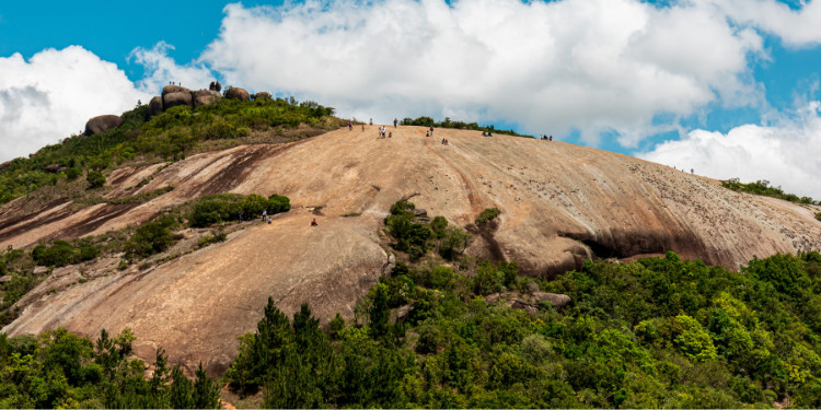 Vista da Pedra Grande em Atibaia, com pessoas caminhando na superfície rochosa e vegetação ao redor.
