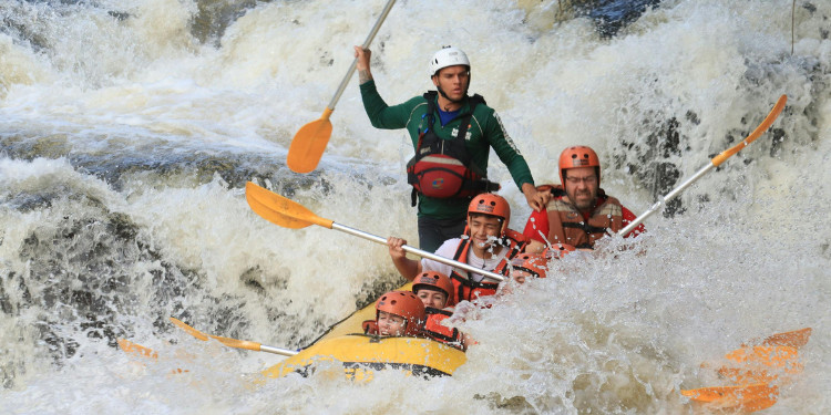 Grupo de pessoas em um bote amarelo fazendo rafting em um rio com corredeiras em Brotas, usando capacetes e coletes salva-vidas.