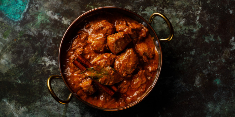 Prato de curry indiano com pedaços de frango em molho espesso em tigela com alças.