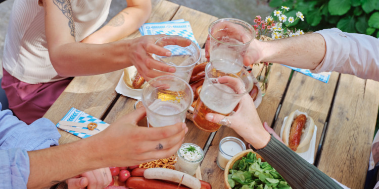 Brinde com cerveja alemã em um ambiente festivo, com foco nas mãos e nas canecas.