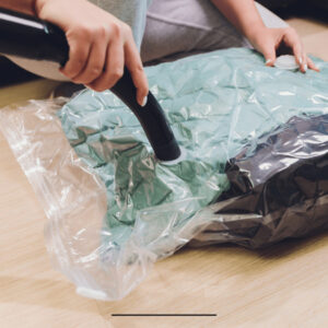 Uma pessoa usando um aspirador de pó para retirar o ar de um saco a vácuo com roupas.