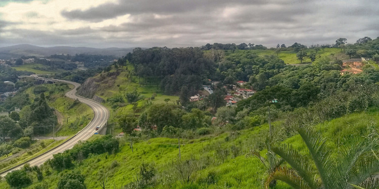 Vista panorâmica de São Roque com estrada sinuosa, montanhas cobertas de vegetação e céu nublado.
