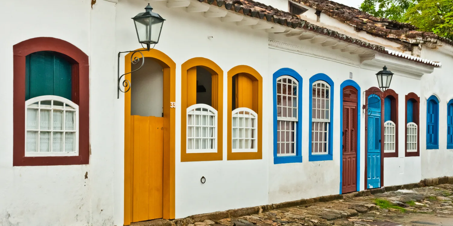 Casas coloniais brancas com portas e janelas em cores vibrantes, como amarelo, azul e vermelho, em uma rua de pedra no centro histórico de Paraty.