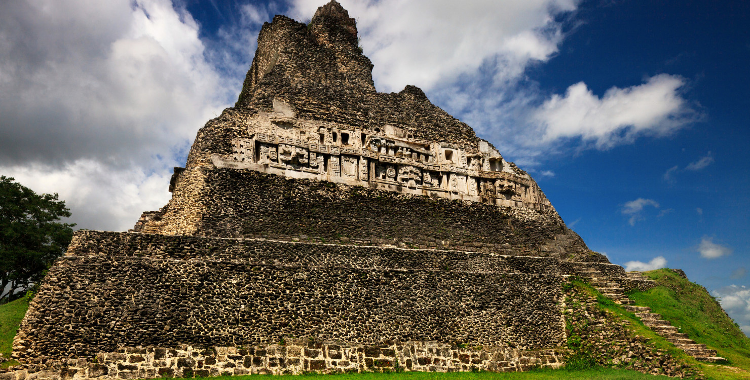 Foto turística da pirâmide maia El Castillo em Xunantunich, Belize, com detalhes da estrutura e vegetação ao redor.
