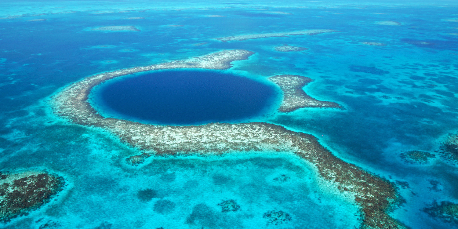 Imagem turística do Grande Buraco Azul em Belize, com destaque para a cor azul profunda da formação e a clareza da água ao redor.
