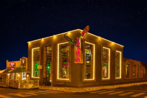 Foto do Brotas Bar à noite, mostrando a fachada iluminada do restaurante com luzes amarelas e detalhes em madeira. As estrelas são visíveis no céu noturno, criando um ambiente charmoso e convidativo.