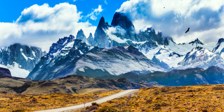 Paisagem da Patagônia Argentina com o Monte Fitz Roy ao fundo, estrada de terra em primeiro plano e céu com nuvens dramáticas.
