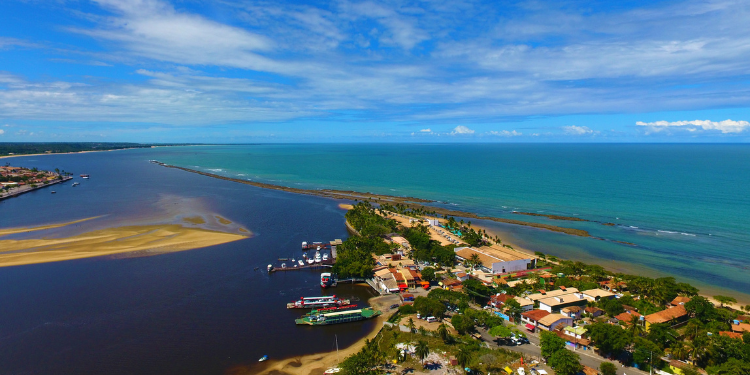 Vista aérea da foz do Rio Buranhém em Porto Seguro, Bahia, mostrando o ponto de travessia da balsa para Arraial d'Ajuda, o encontro do rio escuro com o mar azul e a orla das cidades.